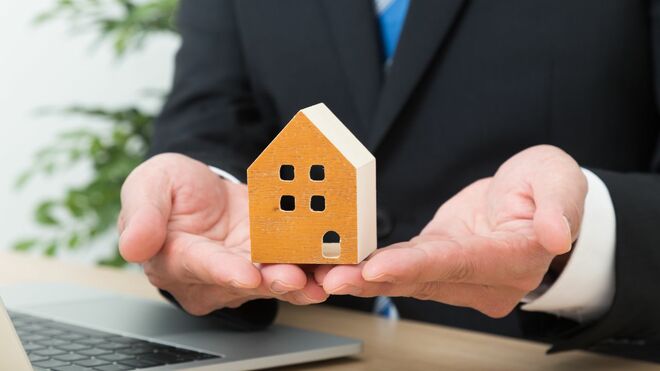 家の模型を両手で持つスーツを着た人物