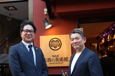 (左から)「BARお酒の美術館」の看板を前に微笑む長田氏と松尾氏