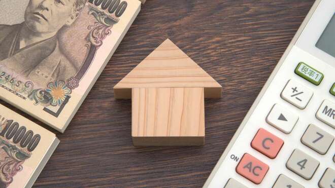 家を模した木のブロックと、それを挟むように置かれた札束・電卓