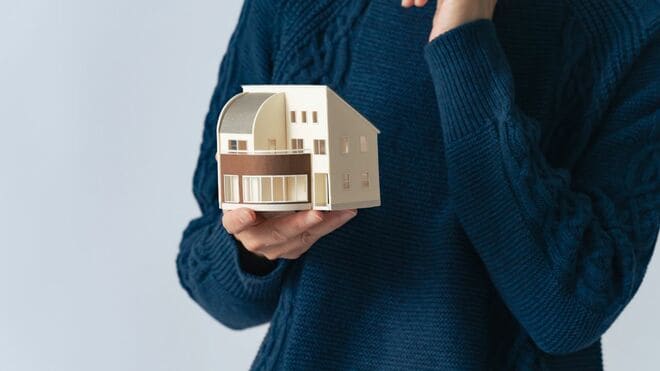 住宅模型を持って顎に手を当てている人